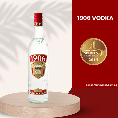 A 700ml bottle of Polmos Lublins 1906 Vodka, renowned for its quadruple distillation, sits on a round wooden platform. The red and white label with a gold shield is accompanied by a 2013 International Spirits Challenge gold medal against a cream and red backdrop with a plant silhouette.